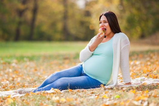 Pregnant woman relaxing in park. She is eating apple.