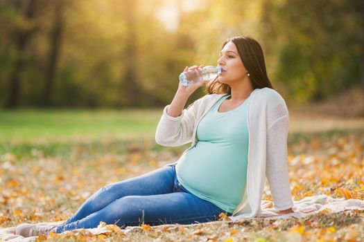 Pregnant woman relaxing in park. She is drinking water.
