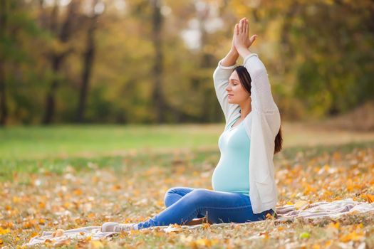 Pregnant woman relaxing in park. She is meditating.