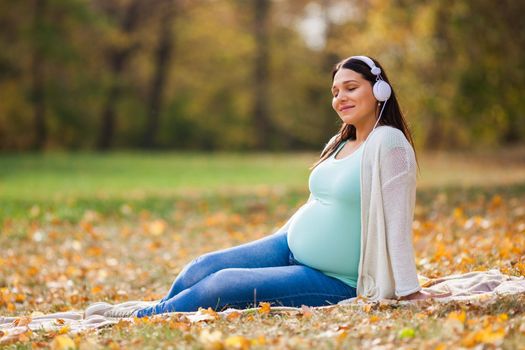 Pregnant woman relaxing in park. She is listening music.