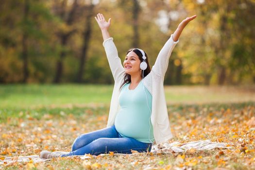 Pregnant woman relaxing in park. She is listening music.