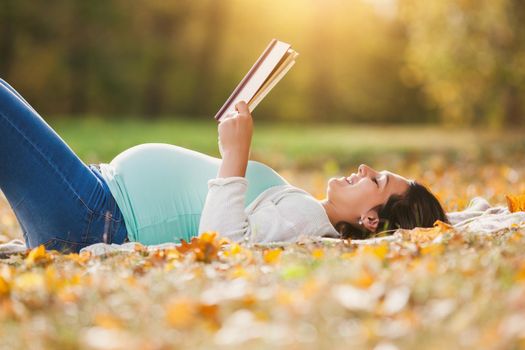 Pregnant woman relaxing in park. She is reading book.