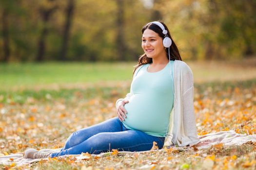 Pregnant woman relaxing in park. She is listening music.