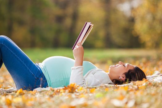 Pregnant woman relaxing in park. She is reading book.