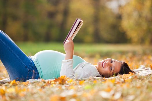 Pregnant woman relaxing in park. She is reading book.