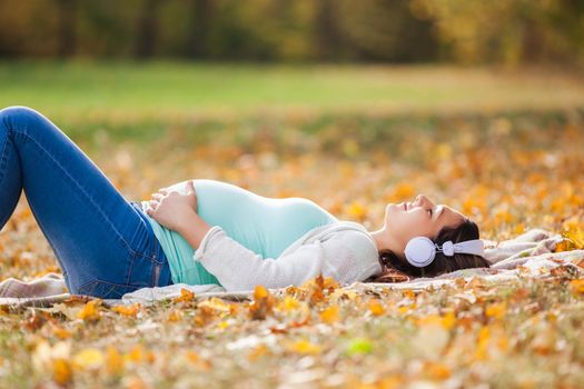 Pregnant woman relaxing in park. She is listening music.