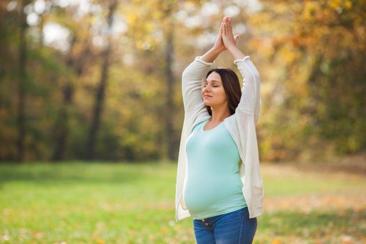 Pregnant woman relaxing in park. She is meditating.