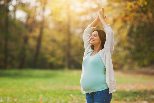 Pregnant woman relaxing in park. She is meditating.