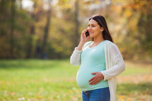 Pregnant woman relaxing in park. She is talking on phone.