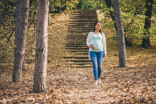 Happy pregnant woman is walking in park.