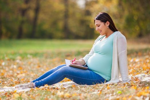 Pregnant woman relaxing in park. She is writing to do list.