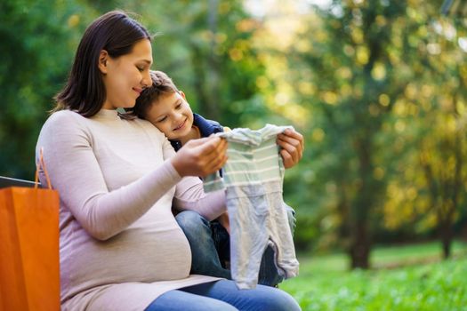 Happy boy and his pregnant mother are are looking at clothes for baby.