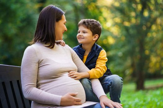 Happy boy and his pregnant mother are enjoying autumn in park.