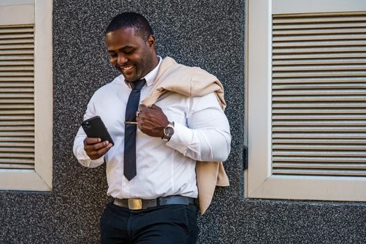 Portrait of happy african-american businessman who is using smartphone.