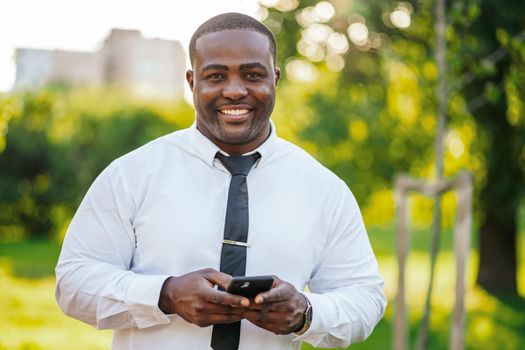 Portrait of happy african-american businessman who is using smartphone.