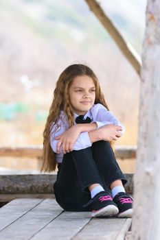 A girl sits on a wooden table and looks into the distance happily and dreamily