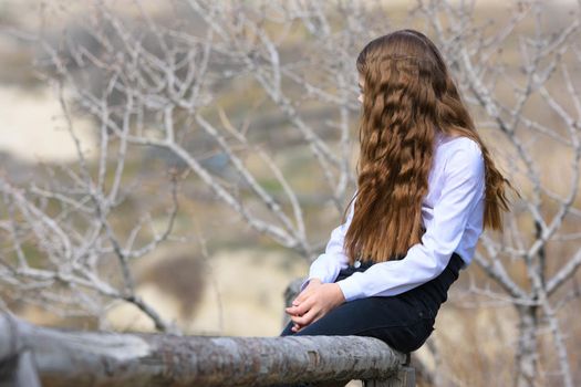 A girl sits on a wooden fence and looks away into the distance