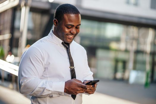 Portrait of happy african-american businessman who is using smartphone.