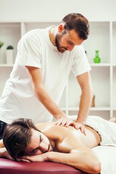 Young man is enjoying massage on spa treatment. Professional masseur is massaging his back.