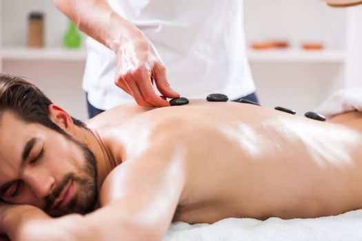 Young man is enjoying hot stone therapy on spa treatment.