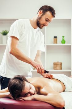 Young man is enjoying massage on spa treatment. Professional masseur is applying massage oil to his skin.