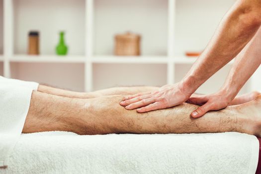 Young man is enjoying massage on spa treatment. Professional masseur is massaging leg of man.