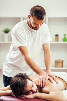 Young man is enjoying massage on spa treatment. Professional masseur is massaging his back.