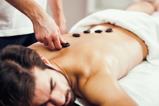 Young man is enjoying hot stone therapy on spa treatment.