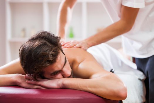 Young man is enjoying massage on spa treatment. Professional masseur massaging back of man.