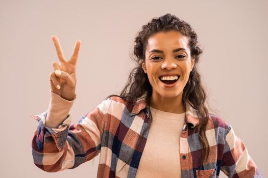 Studio shot portrait of beautiful happy african-american ethnicity woman in casual clothing showing victory hand sign.