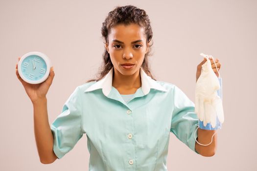 Portrait of serious nurse who is holding protective workwear and clock that shows five to twelve time.