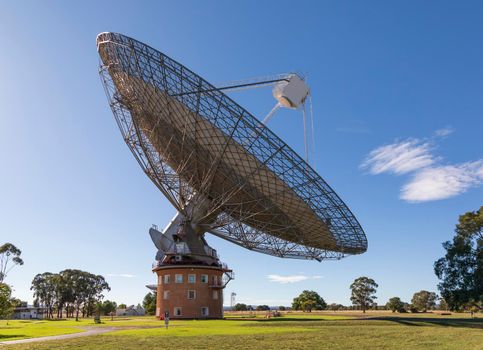 A large outdoor scientific radio telescope in the sunshine in a green field with trees