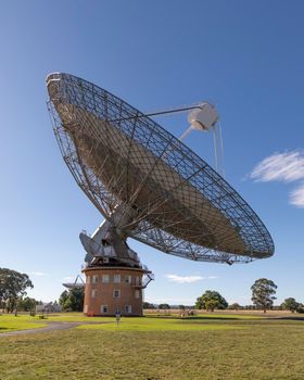 A large outdoor scientific radio telescope in the sunshine in a green field with trees