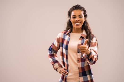 Studio shot portrait of beautiful happy african-american ethnicity woman in casual clothing showing thumb up.
