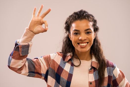 Studio shot portrait of beautiful happy african-american ethnicity woman in casual clothing showing ok hand sign.