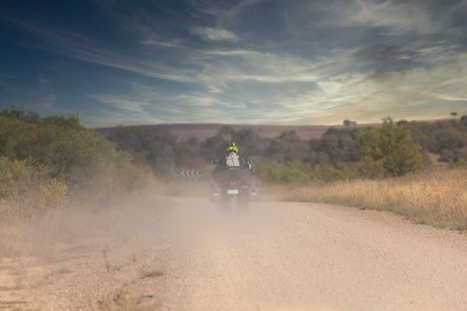 A person riding a motorcycle into the distance on a dusty dirty road