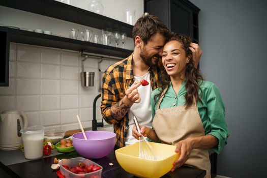 Happy multiracial couple cooking in their kitchen. They are making cookies and having fun.