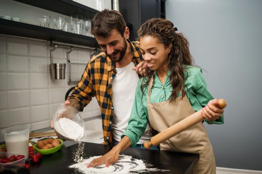 Happy multiracial couple cooking in their kitchen. They are making cookies and having fun.