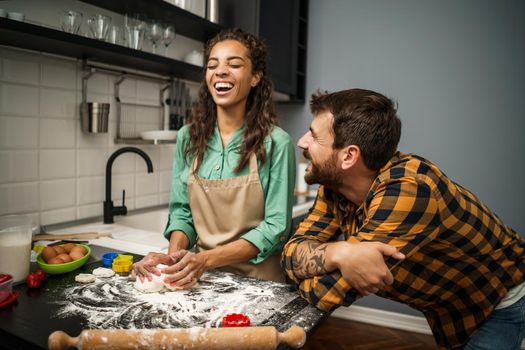Happy multiracial couple cooking in their kitchen. They are making cookies.