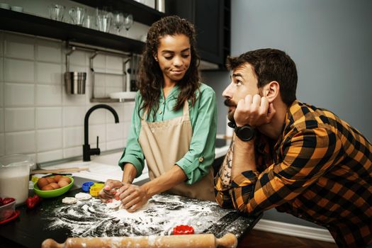 Young multiracial couple cooking in their kitchen. They are making cookies.