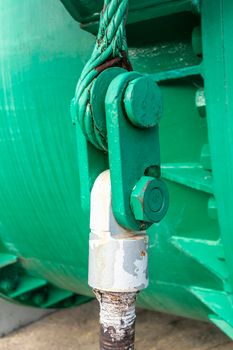 Close up view of of an old green steel shackle with a large nut and rusty steel cable