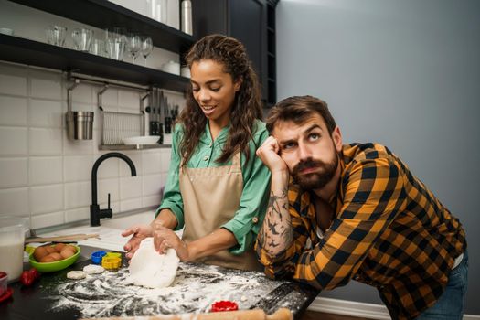 Young multiracial couple cooking in their kitchen. They are making cookies.