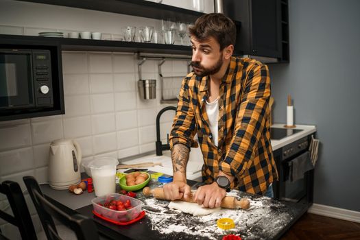 Young man is making cookies in his kitchen. He is tired and bored.