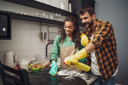 Happy multiracial couple is cleaning their kitchen and having fun.