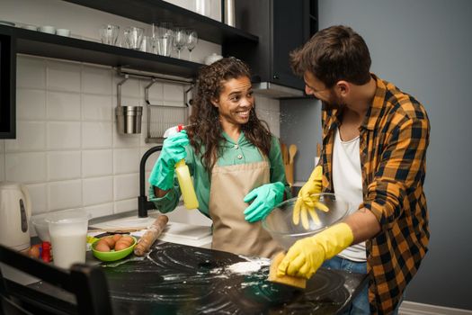 Happy multiracial couple is cleaning their kitchen and having fun.