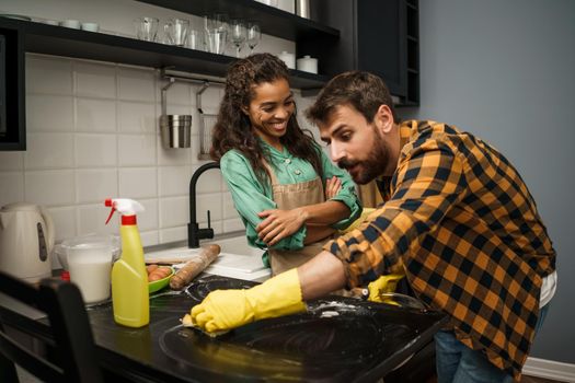 Young multiracial couple is cleaning their kitchen. Woman is lazy and man is angry.