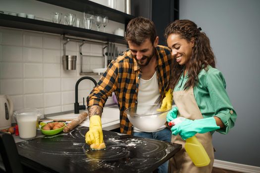 Happy multiracial couple is cleaning their kitchen and having fun.