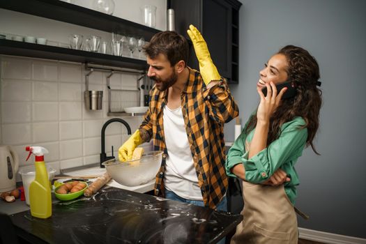 Young multiracial couple is cleaning their kitchen. Woman is lazy and man is angry.