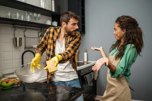 Young multiracial couple is cleaning their kitchen. Woman is lazy and man is angry.