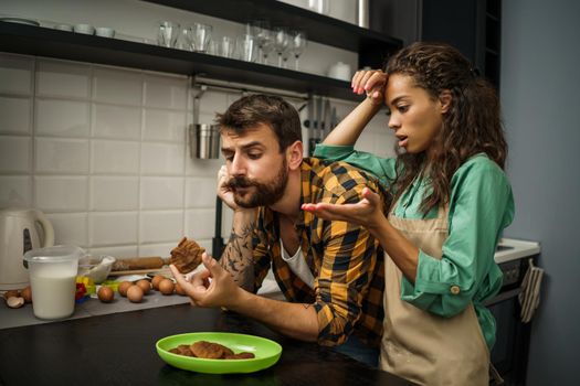 Multiracial couple is unhappy because cookies they have made are burnt.
